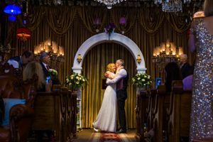 Wedding ceremony under ornate arch with crystal chandeliers and mood lighting.