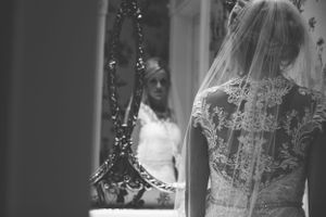 Black and white reflection of bride's lace dress details in ornate vintage mirror.