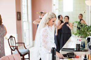 Bride in lace gown stands in elegant room with bridesmaids in navy dresses.