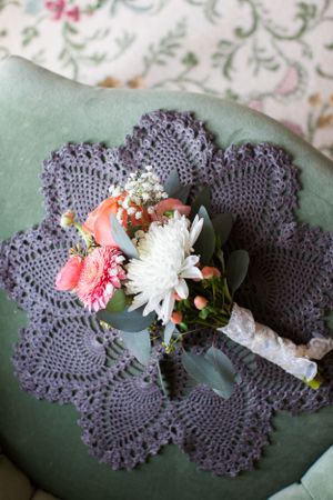 Wedding bouquet with coral and white flowers resting on purple crocheted doily.