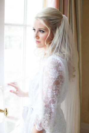 Bride in lace sleeve gown poses by window in elegant bridal portrait.