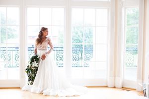 Wedding dress silhouette against bright windows and ornate balcony details.