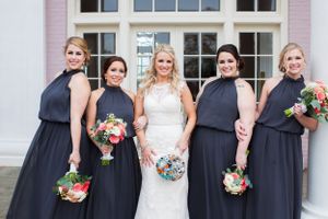 Wedding party in navy blue dresses holding colorful bouquets poses with bride in white.