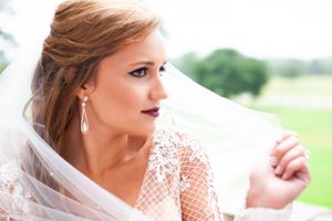A close-up view of a bride wearing a lace veil and elegant earrings outdoors.