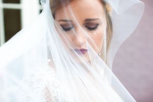 Ethereal bridal portrait through sheer veil with soft makeup and romantic lighting.