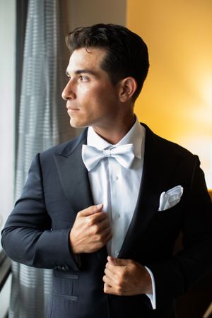 Classic black tuxedo with white bow tie and pocket square in window light.