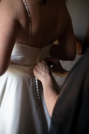 Close-up detail of buttons being fastened on back of white wedding dress.