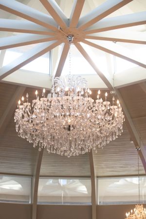 A grand crystal chandelier hangs from a vaulted ceiling with architectural wooden beam details.