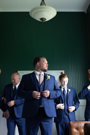 A group in matching navy blue suits stand together in a room with dark green walls and vintage lighting.