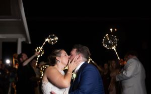 A romantic nighttime sparkler kiss celebration with guests holding lit sparklers in the background.
