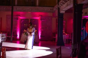 A couple dances in a dramatic spotlight with pink uplighting in an elegant venue.