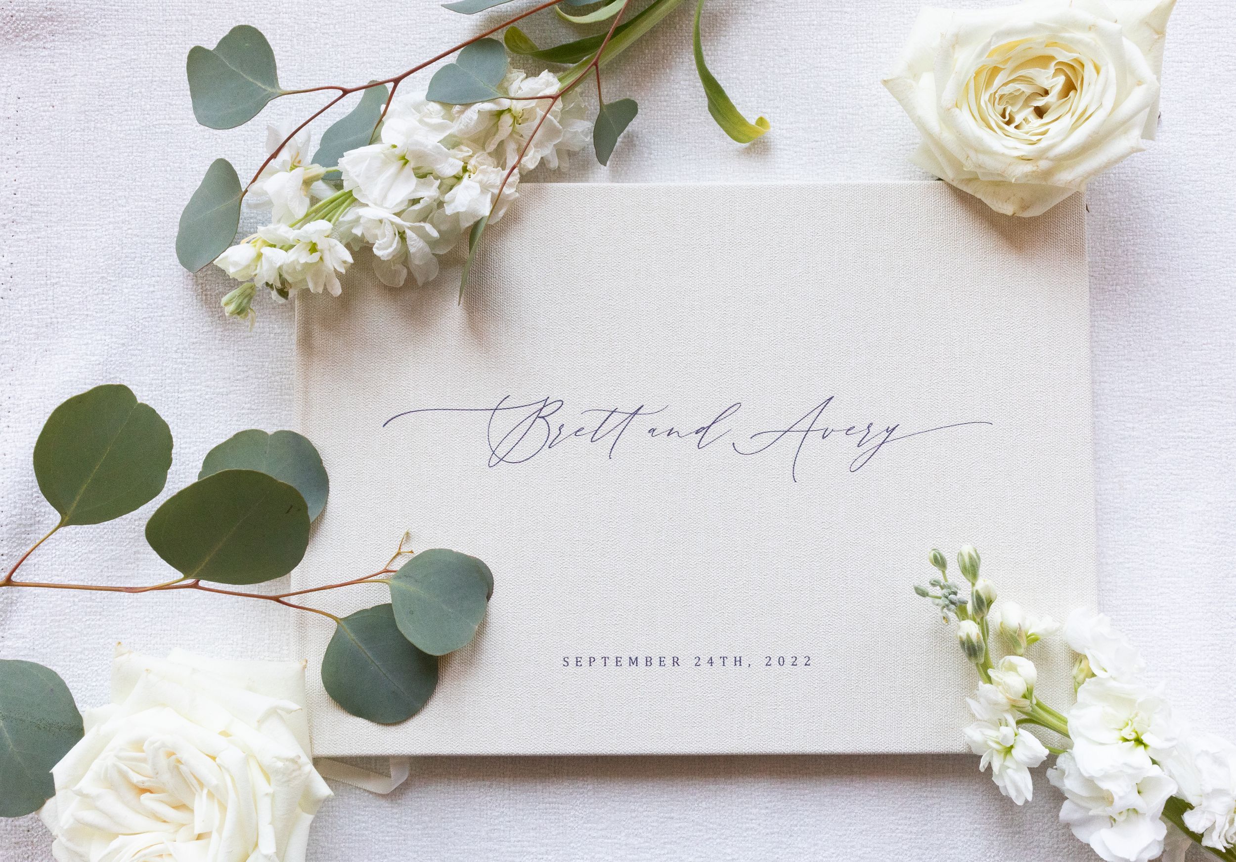 Wedding stationery with calligraphy surrounded by white roses and eucalyptus leaves.