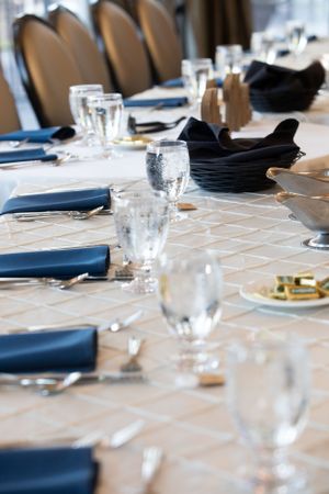 An elegant wedding reception table set with navy blue napkins, crystal glasses, and formal place settings.