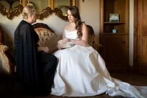 A special moment as a bride in a white wedding gown sits on an ornate sofa reading a note.