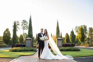 Elegant wedding portrait in front of tall cypress trees and manicured gardens.