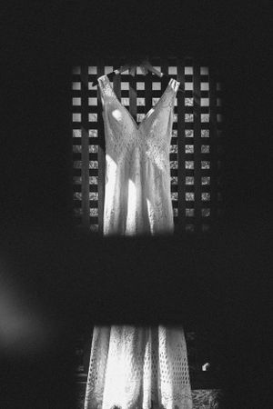 Elegant white lace wedding dress hanging on display against a black grated background in dramatic lighting.
