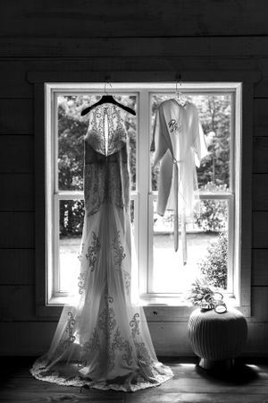 Two wedding dresses displayed in a window frame against dark wooden walls in black and white.