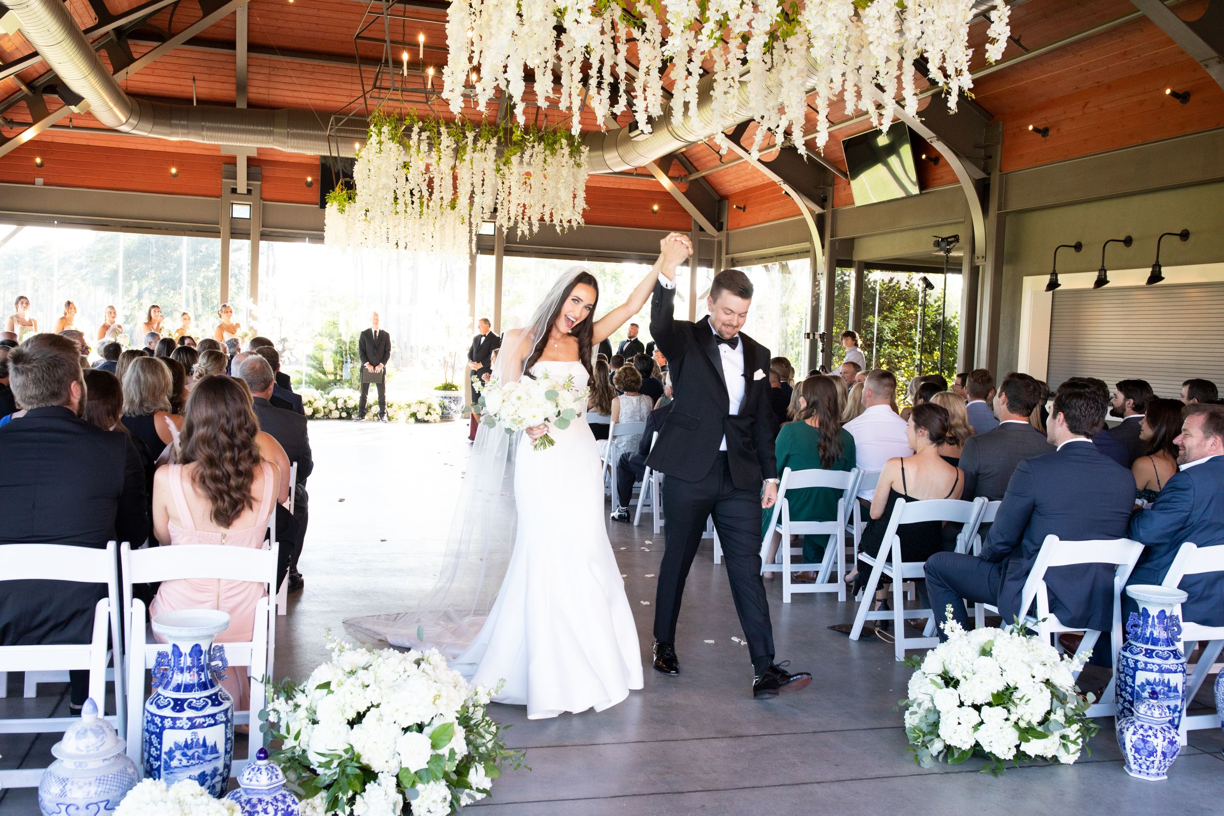 Wedding celebration in outdoor venue with crystal chandeliers and white floral arrangements.