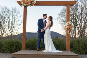 Newlyweds share a romantic kiss under a wooden arch at sunset with mountains in the background.