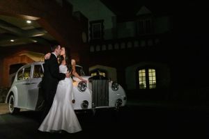 Romantic nighttime portrait with classic white Rolls Royce at venue entrance.