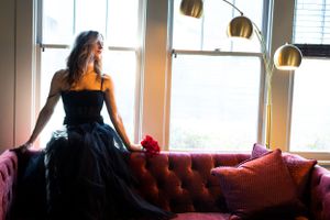 Silhouette of a person in a black gown sitting on a red velvet couch near windows.