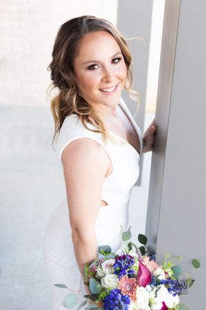 A colorful bridal bouquet with purple and white flowers held near a bright window.