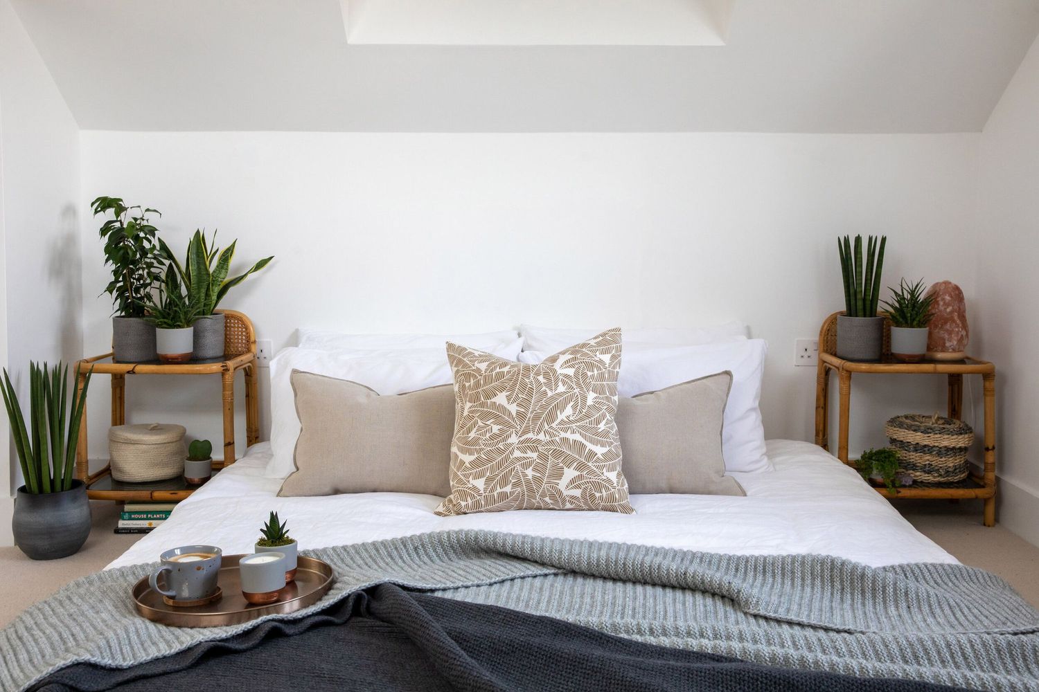 Minimalist bedroom with white bedding, gray throw blanket, and wooden side tables holding plants.