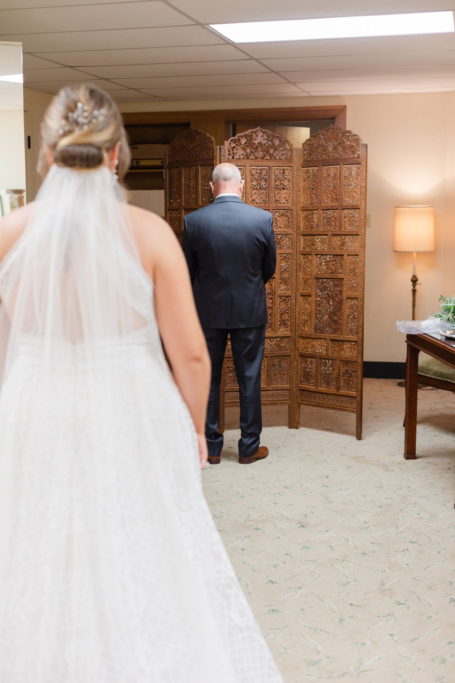 Wedding dress train trailing behind as bride walks across carpeted room.
