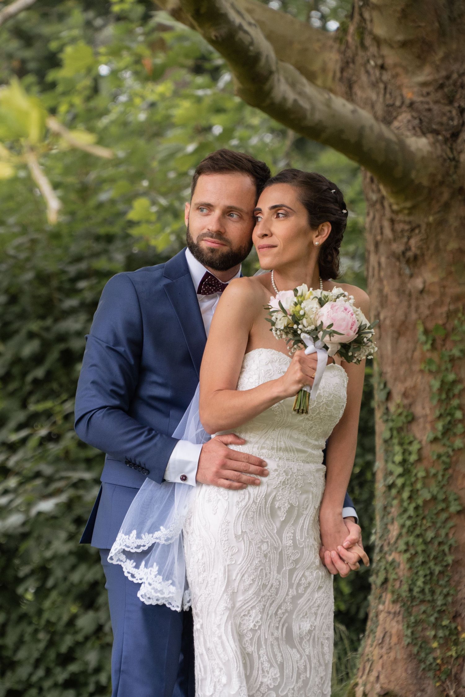 Romantic garden wedding portraits with couple embracing near ivy-covered trees.