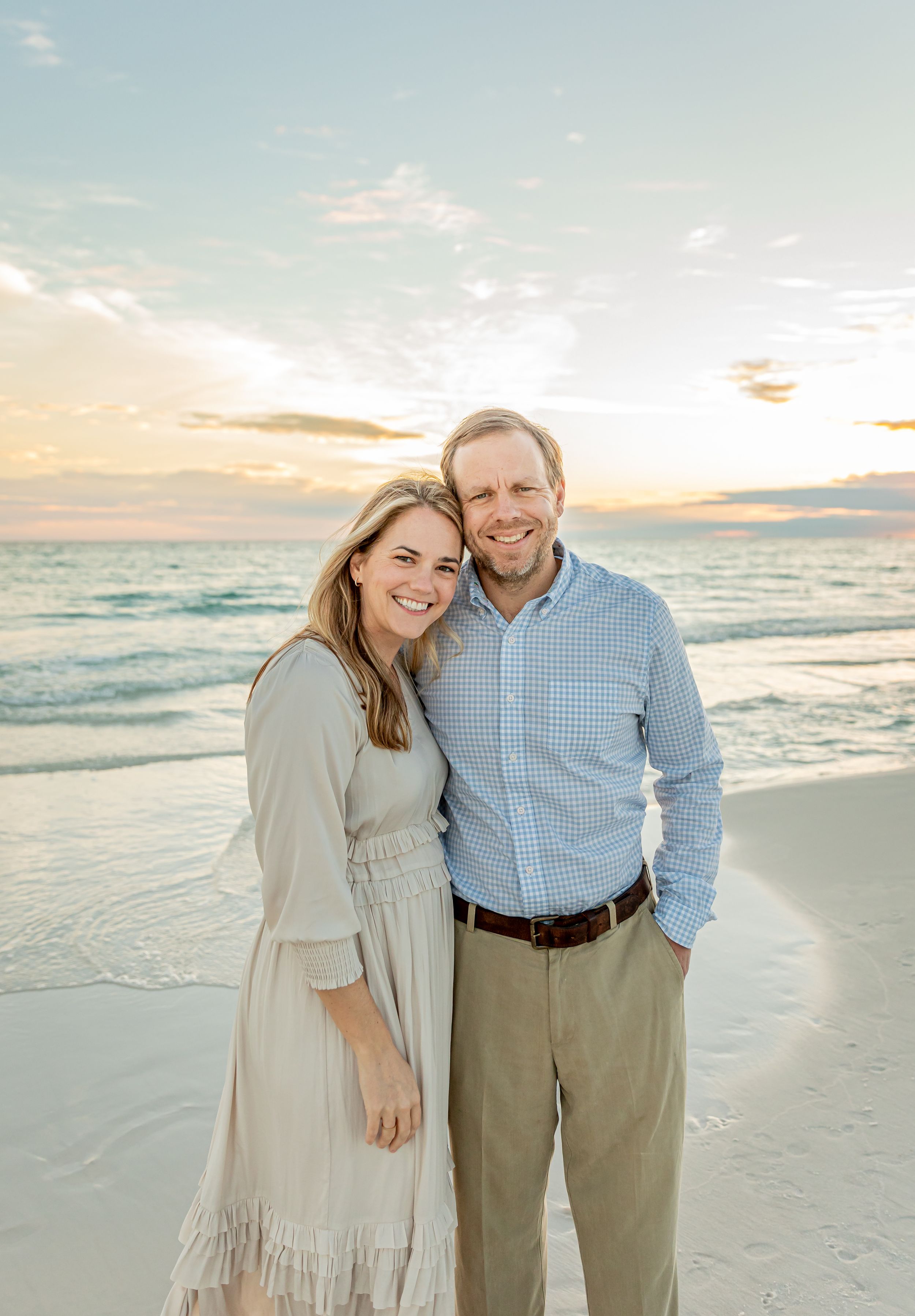 A couple poses together at sunset on a peaceful beach with waves in the background.