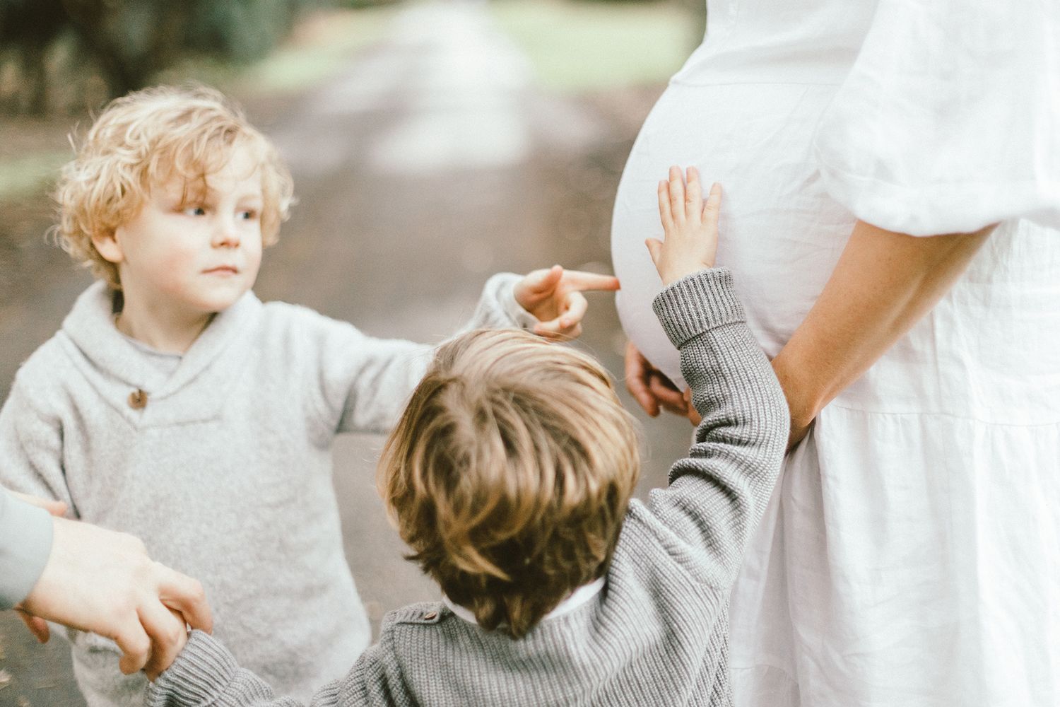 Sweet moments captured between a child and expectant mother in white dress during outdoor photoshoot.