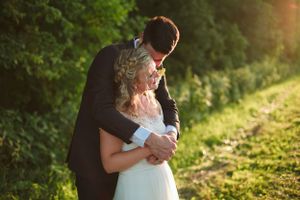 A romantic sunset embrace between newlyweds in a lush green garden setting.