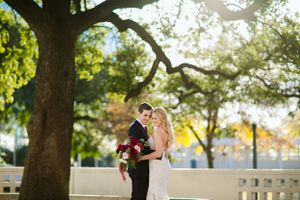 Wedding couple embracing under a large oak tree with sunlight filtering through.