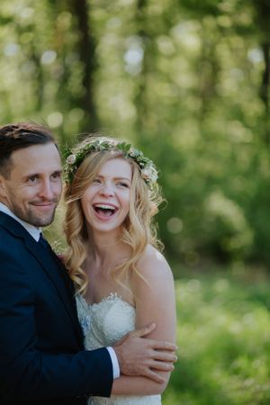 A joyous wedding couple share an intimate moment in a sunlit forest setting.