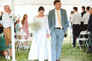 Wedding ceremony procession in a tented outdoor venue with elegant white decor.