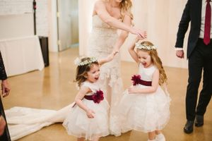 Flower girls in white dresses with burgundy sashes playing at wedding reception.