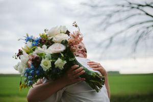 A close-up of hands holding a vibrant wedding bouquet with white, blue and pink flowers.