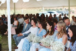 Wedding guests seated under a white tent holding baby's breath bouquets.
