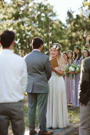 An outdoor wedding ceremony with bridesmaids in lavender dresses and floral crowns.