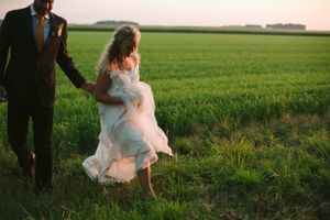 A couple walking through a green field during sunset, with the bride's dress flowing in the breeze.