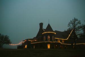 Historic Victorian mansion illuminated with string lights against dusky sky.
