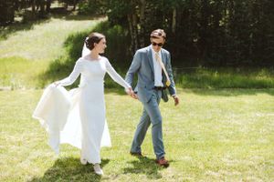 A couple walks hand in hand through a sunny mountain meadow on their wedding day.