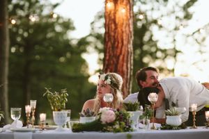 A romantic table setting in a forest with pink flowers and glowing candlelight.