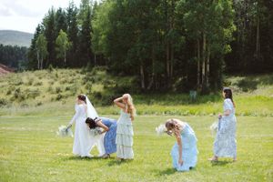 Wedding party members in flowing dresses dance across a sunny meadow.