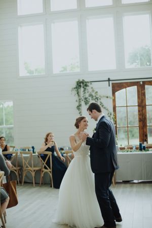 A couple sharing their first dance in a bright, airy venue with high windows and wooden floors.