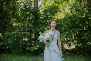 A candid moment of joy in a garden setting with a simple bouquet and light blue dress.