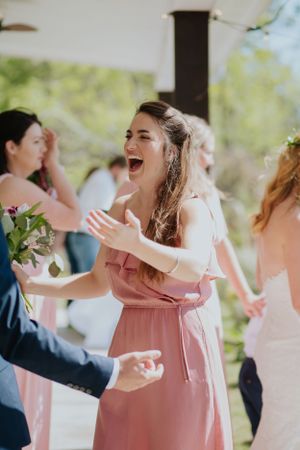 Bridesmaid in pink dress laughing joyfully during wedding celebration.