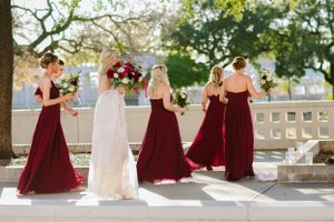 Bridal party in burgundy dresses walking along outdoor terrace.