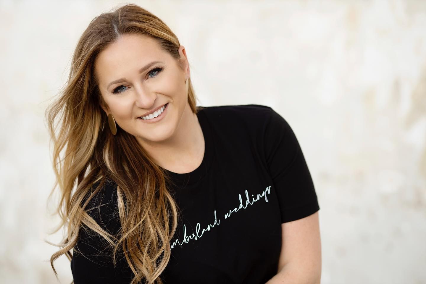 Studio portrait of a woman with long hair wearing a black t-shirt against a light background.