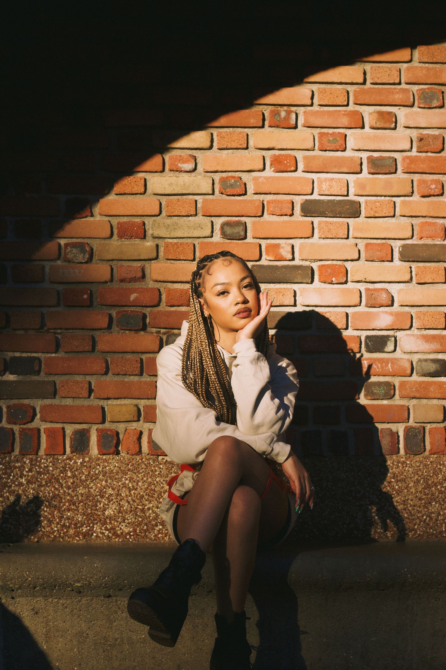 Singer/songwriter Juani sitting on a bench in front of a brick wall during sunset in Queens NY.